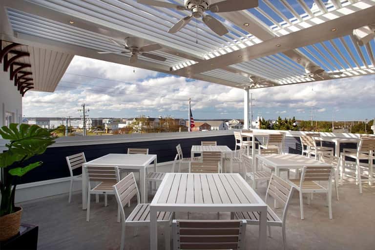 Rooftop dining area with white pergola, ceiling fans, tables, chairs, and waterfront views