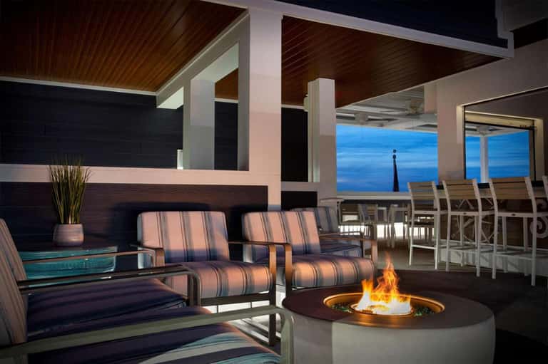 Oceanfront terrace with fire pit, striped seating, wooden ceiling, and blue water views at dusk