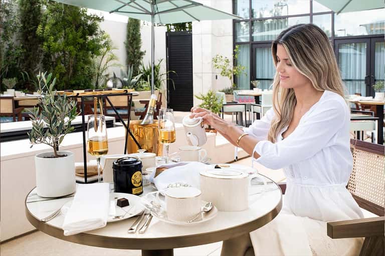 Woman enjoying tea at round outdoor dining table on upscale rooftop terrace with greenery