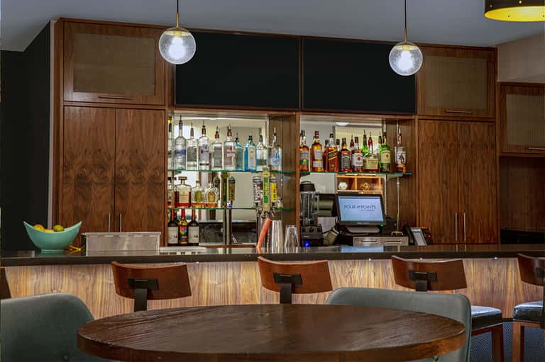 Mid-century modern bar with wood cabinetry, glass shelving, liquor bottles, and round dining table