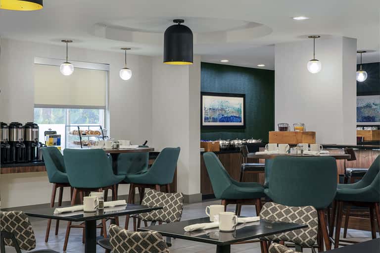 Modern hotel breakfast dining area with teal chairs, pendant lights, and green accent wall featuring artwork