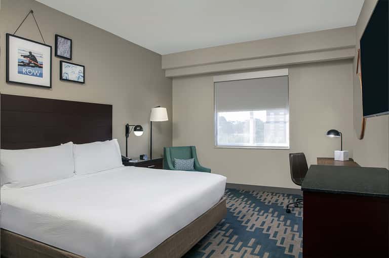Hotel guest room with queen bed, dark headboard, work desk, and city view from window