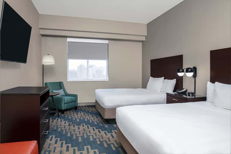 Hotel room with two queen beds, dark wood furniture, and city skyline view