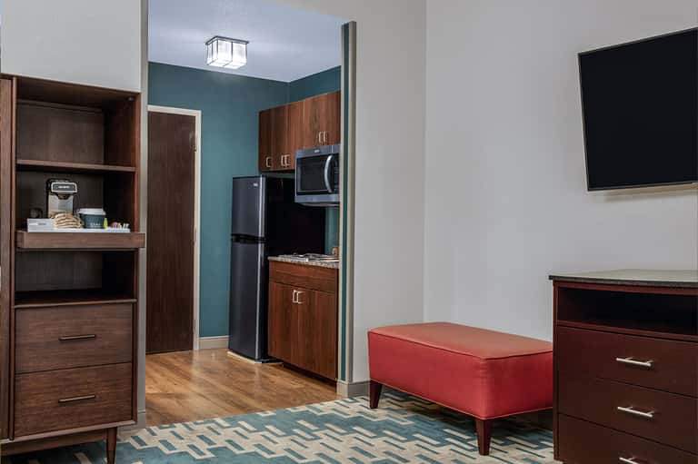 Hotel suite kitchenette with dark wood cabinetry, black appliances, teal accent wall, television