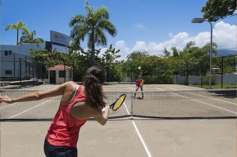 Woman playing tennis on outdoor court with mountains visible in background and palm trees