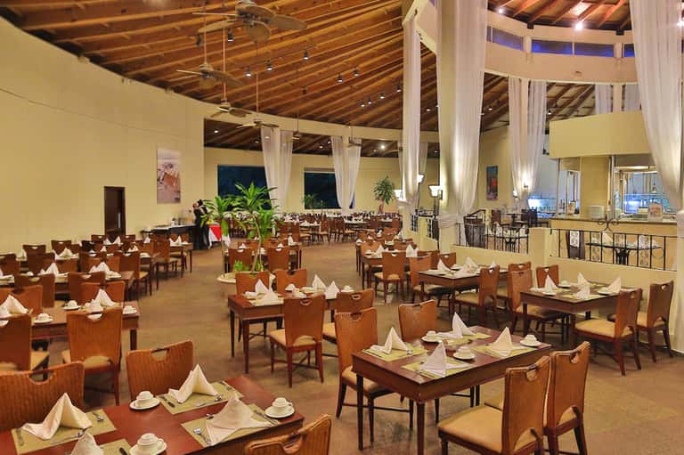 Elegant dining room with wooden chairs, white linens, exposed wooden ceiling, and tall curtains