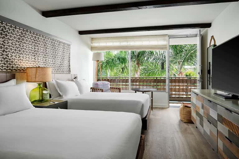 Modern hotel room with two queen beds, balcony with palm trees, and flat-screen TV