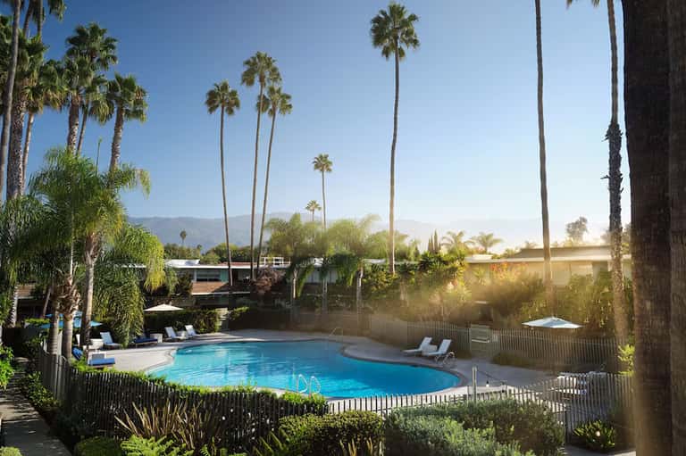 Resort swimming pool with lounge chairs, palm trees, and mountain views in background