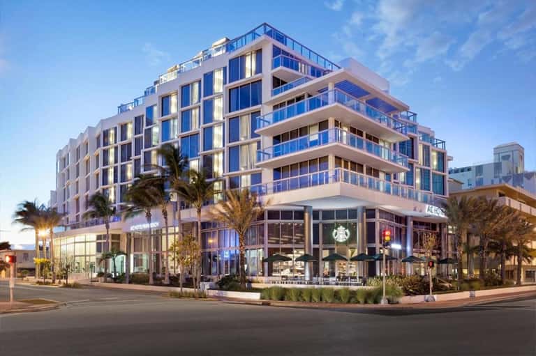 Contemporary multi-story hotel building with blue-tinted glass balconies and ground-level retail storefronts
