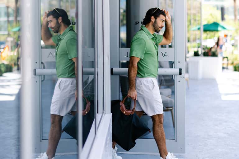 Man in green polo shirt and white shorts entering glass doors of a modern building
