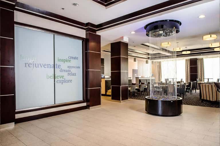 Modern hotel entrance with inspirational words on glass doors, cylindrical water feature, and contemporary design