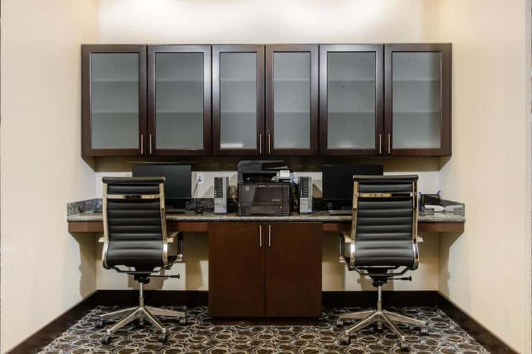 Modern office workspace with dark wood cabinets, dual monitors, and ergonomic black chairs