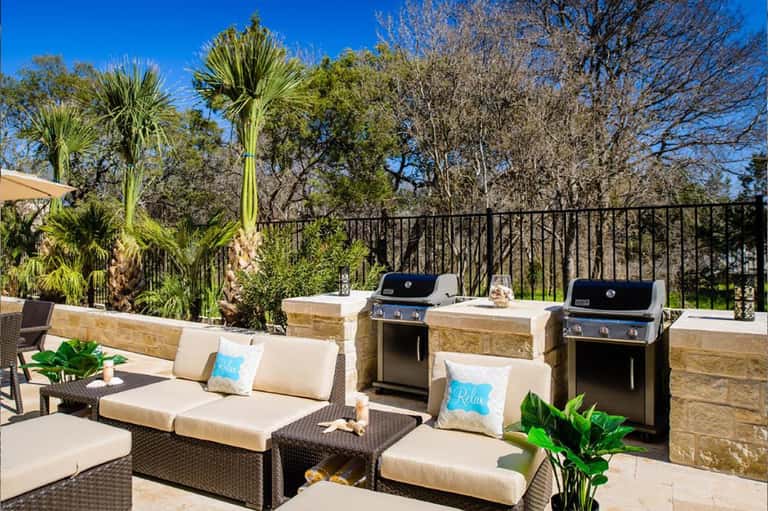 Outdoor patio lounge with cream cushioned seating, stone fire pits, grills, and palm trees