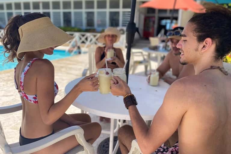 Couple toasting drinks at poolside bar table with umbrellas and lounge chairs