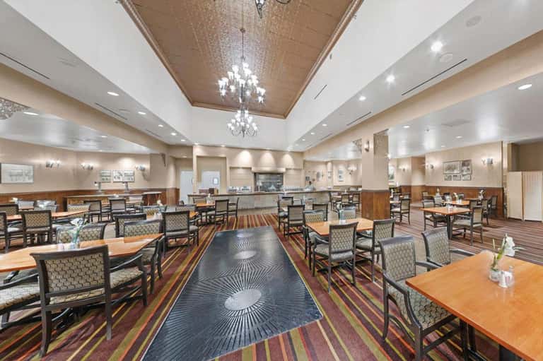 Modern hotel dining room with wood accents, chandeliers, striped carpet, and wooden tables