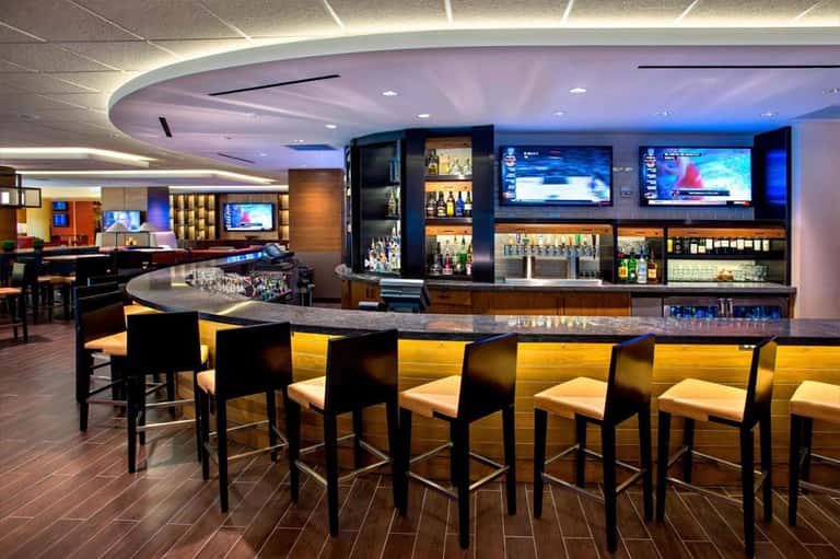 Contemporary hotel bar with curved ceiling, multiple TV screens, and elegant seating
