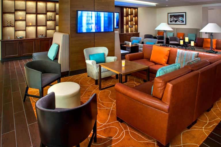 Modern hotel lounge with orange leather seating, wood accents, blue lighting, and geometric patterned flooring