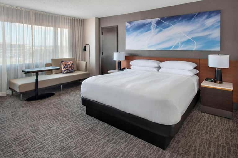 Modern hotel bedroom with queen bed, work desk, and floor-to-ceiling windows