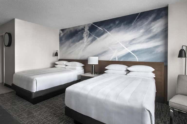 Hotel room with two queen beds, white linens, and abstract sky artwork
