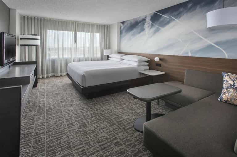 Modern hotel room with queen bed, sofa, flat-screen TV, and mountain view