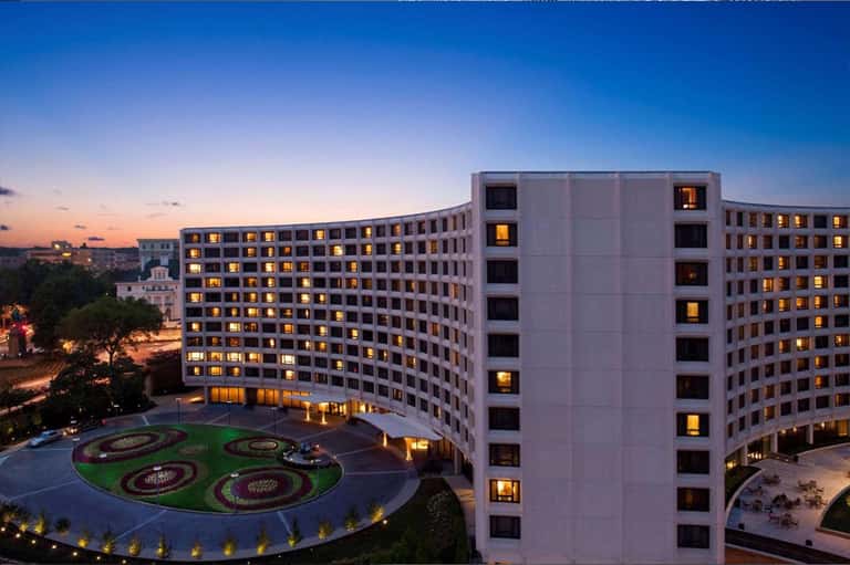 Modern hotel building at dusk with illuminated windows and decorative courtyard gardens