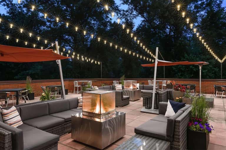 Nighttime rooftop patio with string lights, fire pit, lounge seating, and red umbrellas