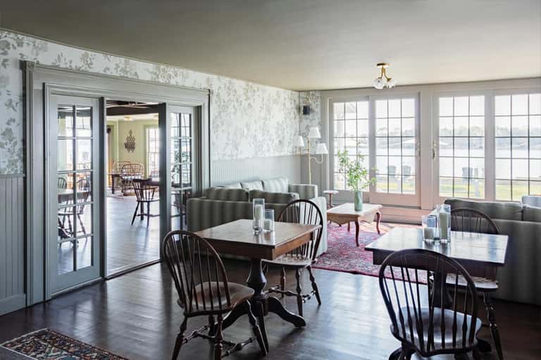 Elegant dining room with fireplace, large windows overlooking water, and classic black Windsor chairs