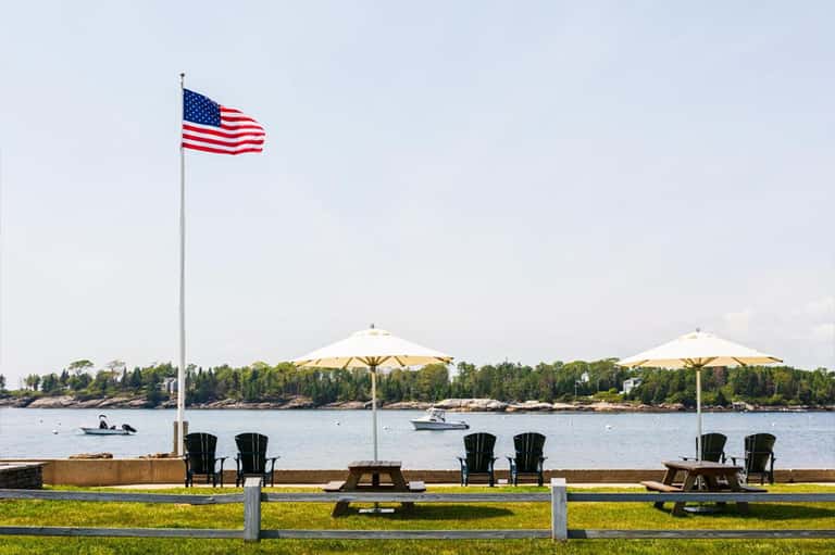 Waterfront picnic area with Adirondack chairs, umbrellas, American flag, and lake views