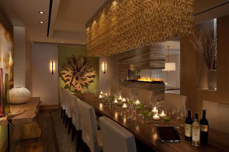 Elegant dining room with golden ceiling feature, fireplace, wine bottles, and long table