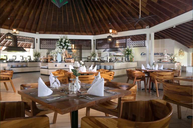 Modern dining room with wooden tables, chairs, and a circular bar under a high wooden ceiling