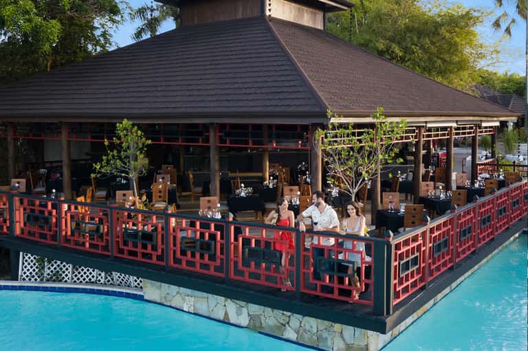Asian-inspired restaurant pavilion with red geometric railings, dark roof, and waterfront seating area