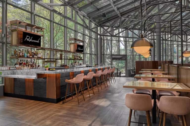Contemporary glass-enclosed restaurant bar with wooden seating and forest views