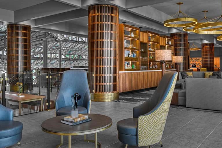 Modern hotel lobby with wooden cylindrical pillars, blue seating, and brass light fixtures
