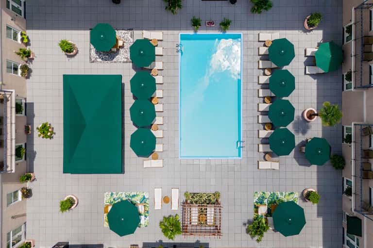 Aerial view of resort pool deck with green umbrellas, loungers, and surrounding tropical vegetation