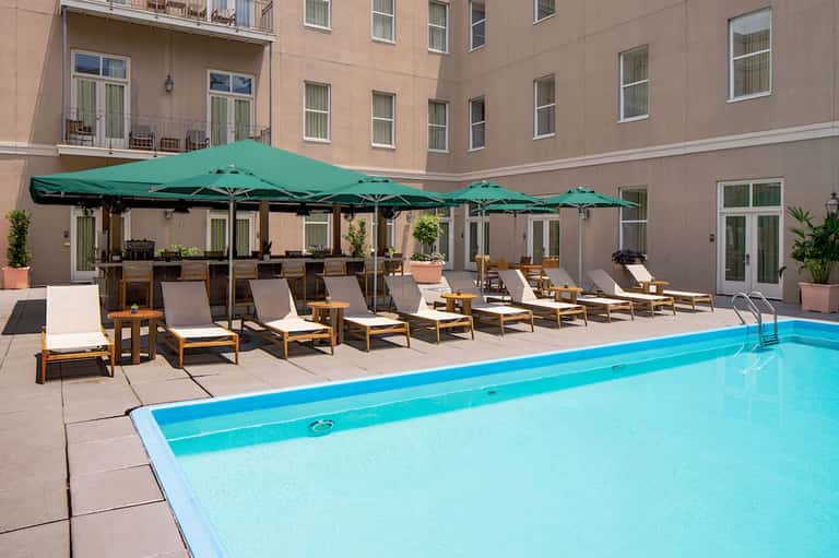 Resort courtyard pool with green umbrellas, wooden lounge chairs, and surrounding hotel building