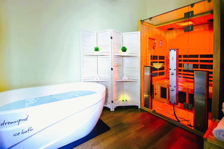 Modern spa room with white ice bath tub, folding screens, and red infrared sauna