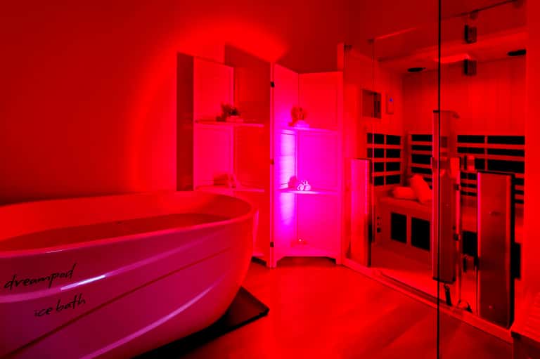 Spa wellness area with red neon lighting, circular bathtub, and glass-enclosed sauna room