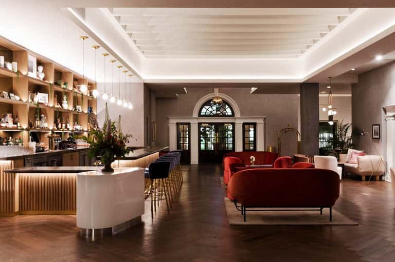 Elegant hotel lobby with red velvet sofa, wooden shelving, curved bar, and modern lighting