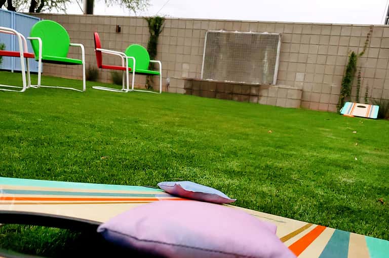 Colorful cornhole game boards on manicured green lawn with soccer goals and brick wall backdrop