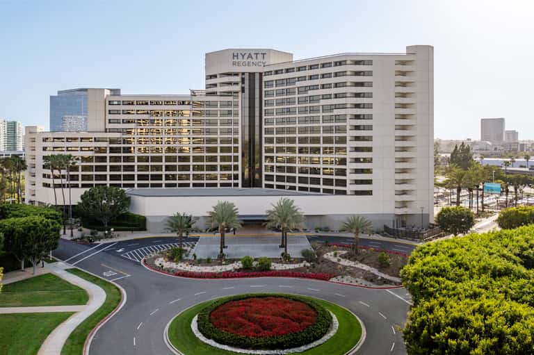 Hyatt Regency hotel exterior with multi-story beige building, manicured landscaping, and palm trees