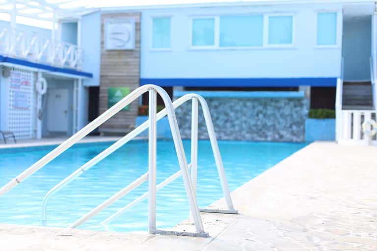 Swimming pool with white ladder and blue water, indoor facility visible in background