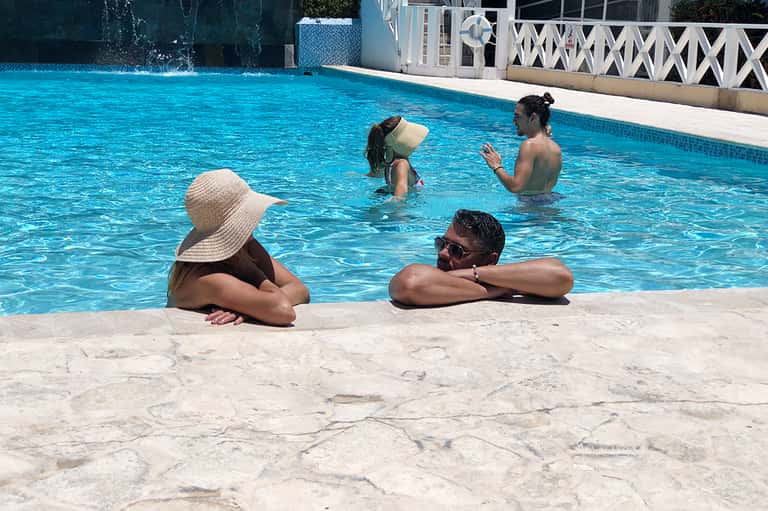 Guests enjoying resort pool with clear turquoise water and white railings on sunny day