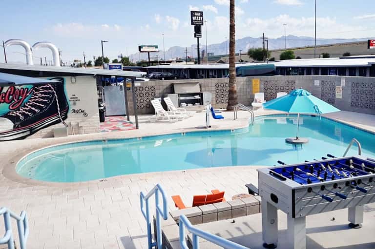 Bright turquoise swimming pool with blue umbrella, lounge chairs, and foosball table on desert landscape