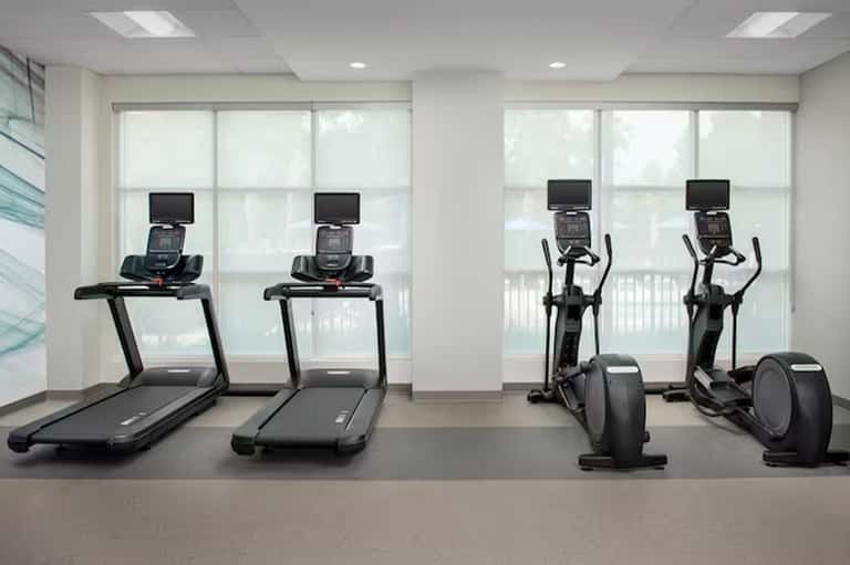 Fitness center with treadmills and elliptical machines facing large windows with natural light