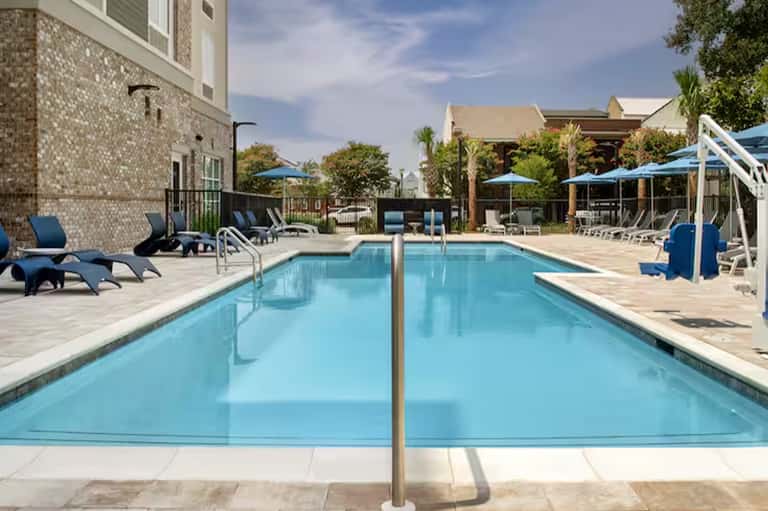 Resort lap pool with clear water, lounge chairs, umbrellas, and brick building
