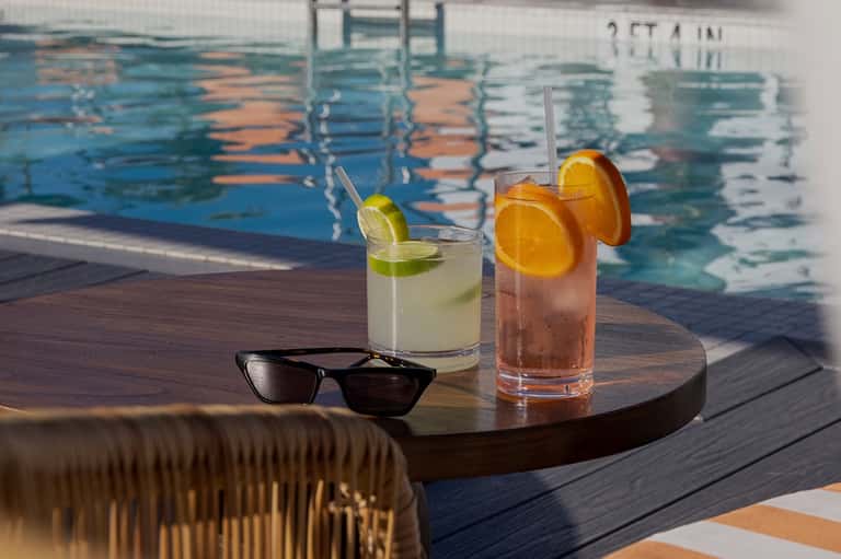 Refreshing cocktails with lime and orange garnish on wooden table by the pool