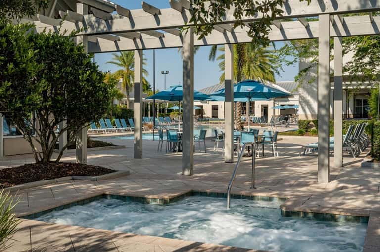 Spa hot tub under pergola with lounge chairs and pool area visible in background