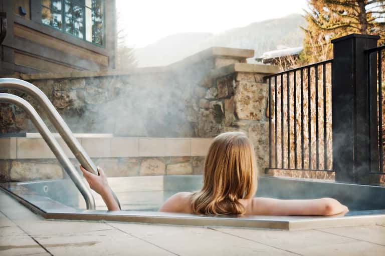 Woman relaxing in outdoor hot spring pool with mountain views and steam rising