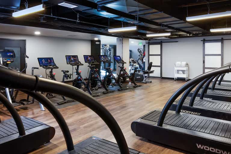 Modern fitness center with treadmills, stationary bikes, and workout equipment on wooden floors