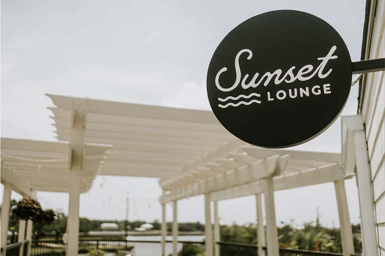 Sunset Lounge signage on white pergola with water view in background